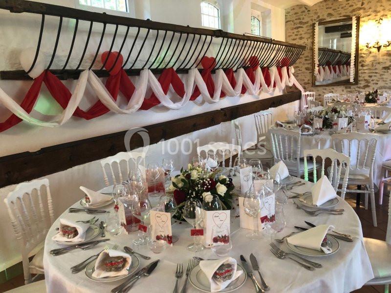 Salle de réception décorée avec des tables rondes dressées, nappes blanches et guirlandes rouges et blanches au mur.
