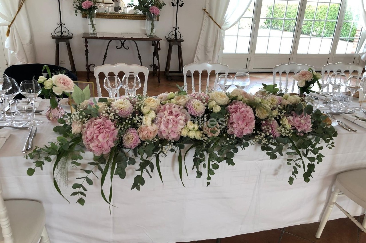 Décoration florale composée de roses et hortensias roses et blancs, disposée sur une table de réception élégante.