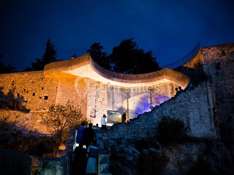 Vue nocturne d'une structure moderne éclairée, intégrée à des ruines en pierre entourées de végétation.