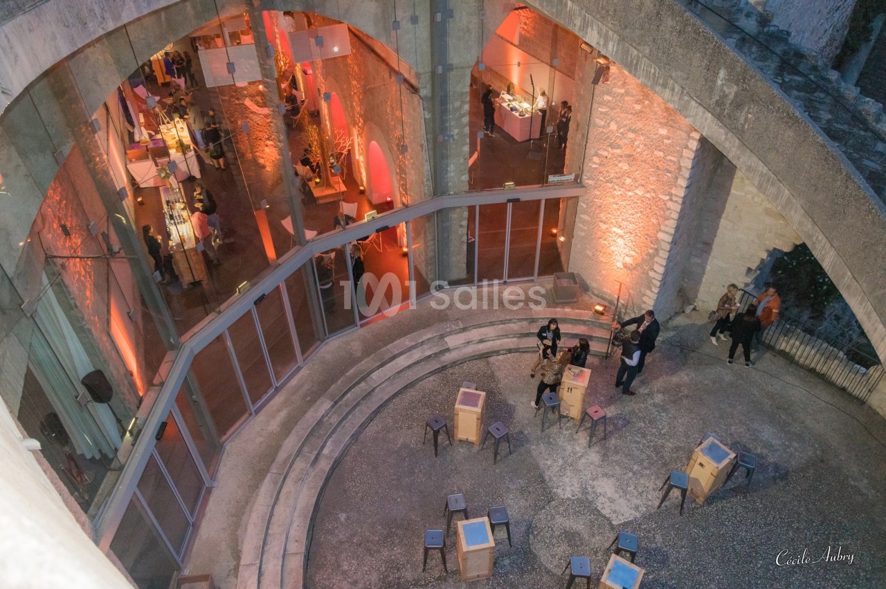 Vue plongeante d'un espace intérieur circulaire avec des arcades, des tables et des visiteurs dans une ambiance lumineuse.