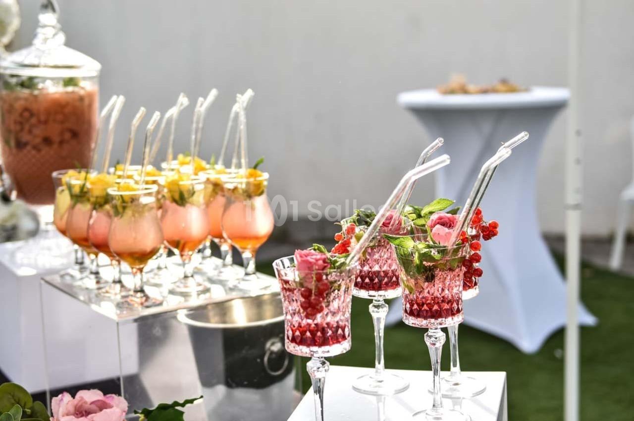 Verres de cocktails colorés garnis de fruits et de feuilles, disposés sur une table lors d'un événement en extérieur.