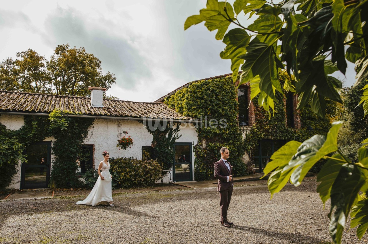 Une mariée s'approche d'un homme en costume dans la cour d'une maison couverte de végétation.
