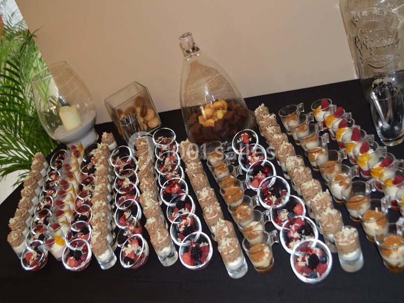Buffet de verrines sucrées variées disposées sur une nappe noire, avec des desserts aux fruits et au chocolat.