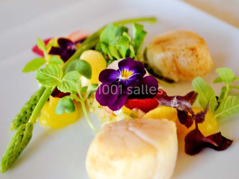 Assiette gastronomique avec noix de Saint-Jacques, asperges, fleurs comestibles et légumes colorés.