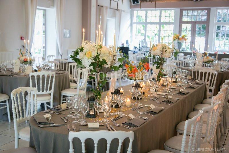 Salle de réception décorée avec des tables élégantes, nappes grises, chandeliers et compositions florales.