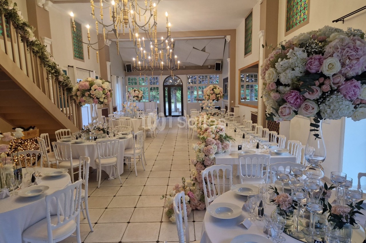 Salle de réception élégamment décorée avec des tables dressées, des chandeliers et des compositions florales pastel.