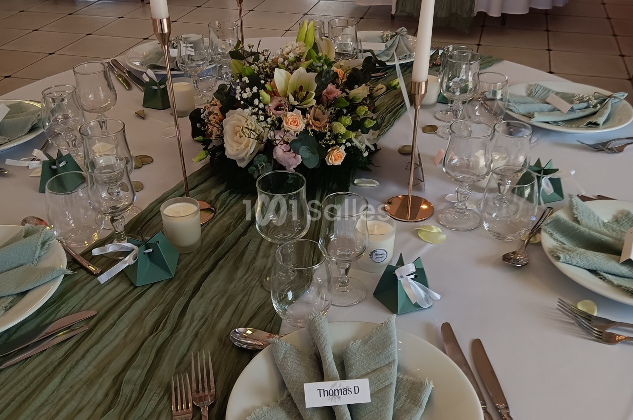 Table élégamment dressée avec nappes vertes, centre de table floral, bougies et pliages de serviettes.