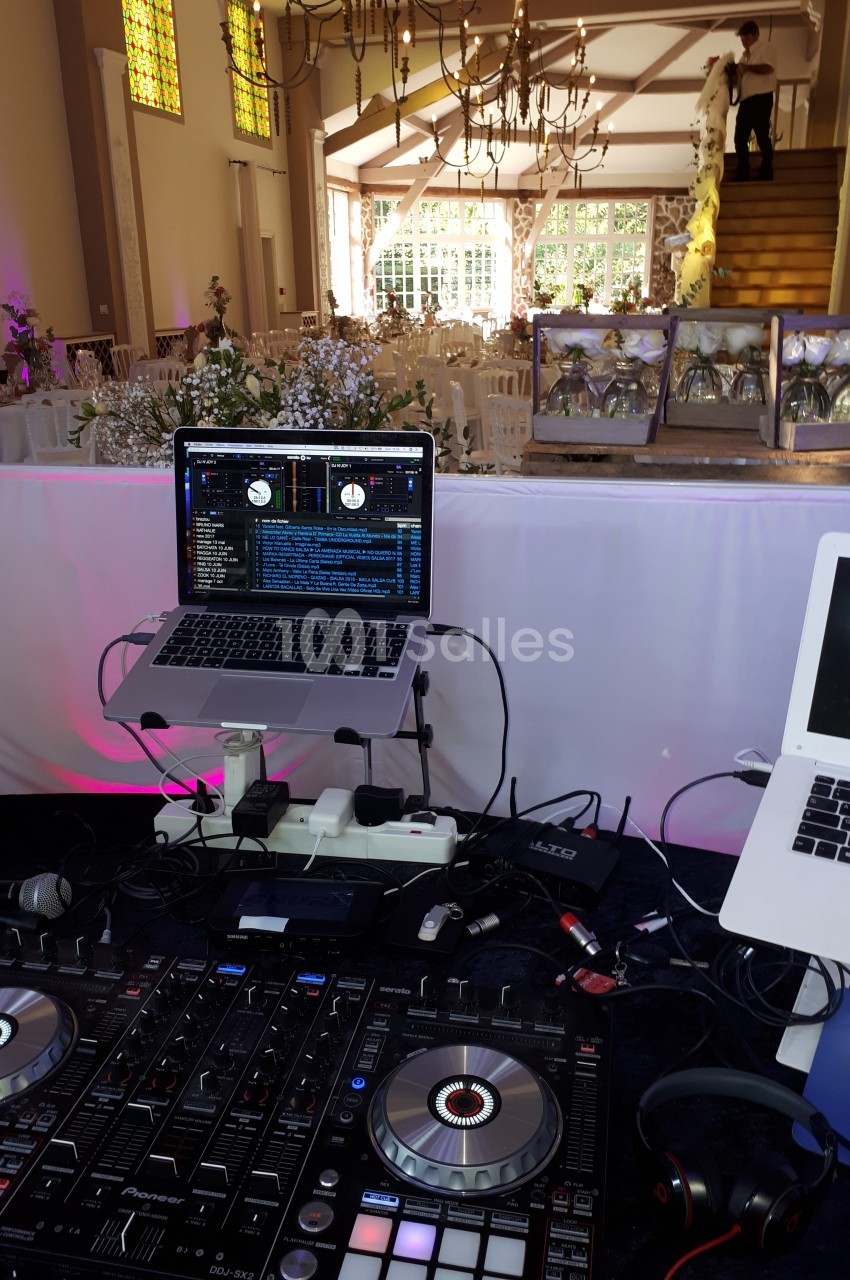 Poste de DJ avec platines et ordinateurs dans une salle de réception décorée pour un mariage.