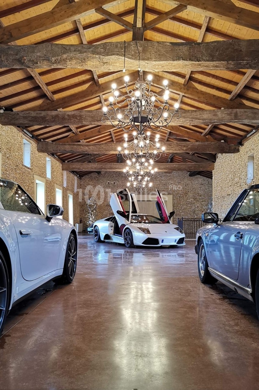 Trois voitures de sport blanches exposées dans une salle en pierre avec un plafond en bois et un grand lustre central.