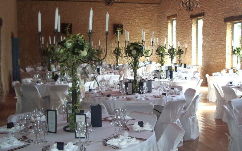 Salle de réception décorée avec des tables rondes, nappes blanches, chandeliers et compositions florales.
