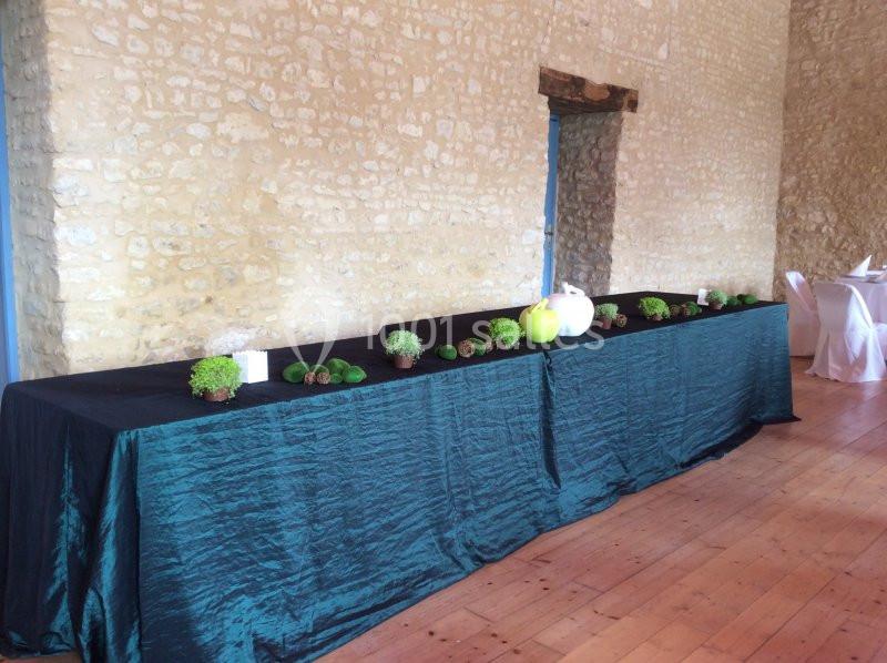 Table longue recouverte d'une nappe verte, décorée de plantes, pommes vertes et éléments naturels, dans une salle en pierre.
