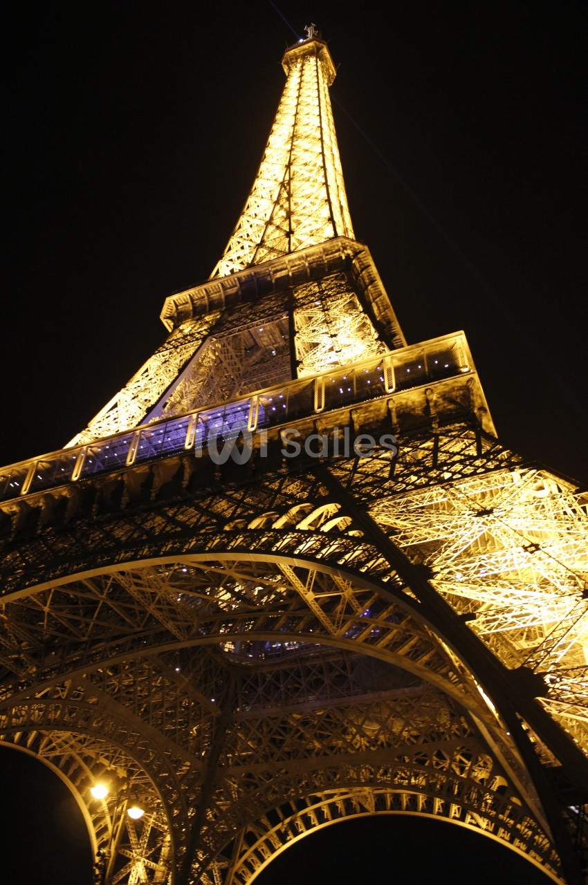 Vue en contre-plongée de la tour Eiffel illuminée la nuit, mettant en valeur sa structure métallique.