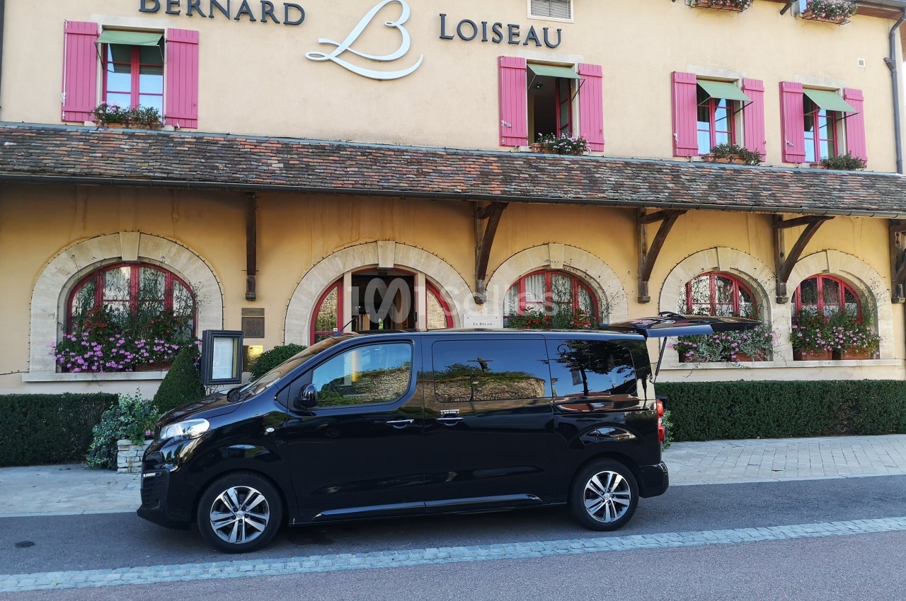 Un véhicule noir stationné devant un bâtiment avec des volets roses et l'enseigne ’Bernard Loiseau’.