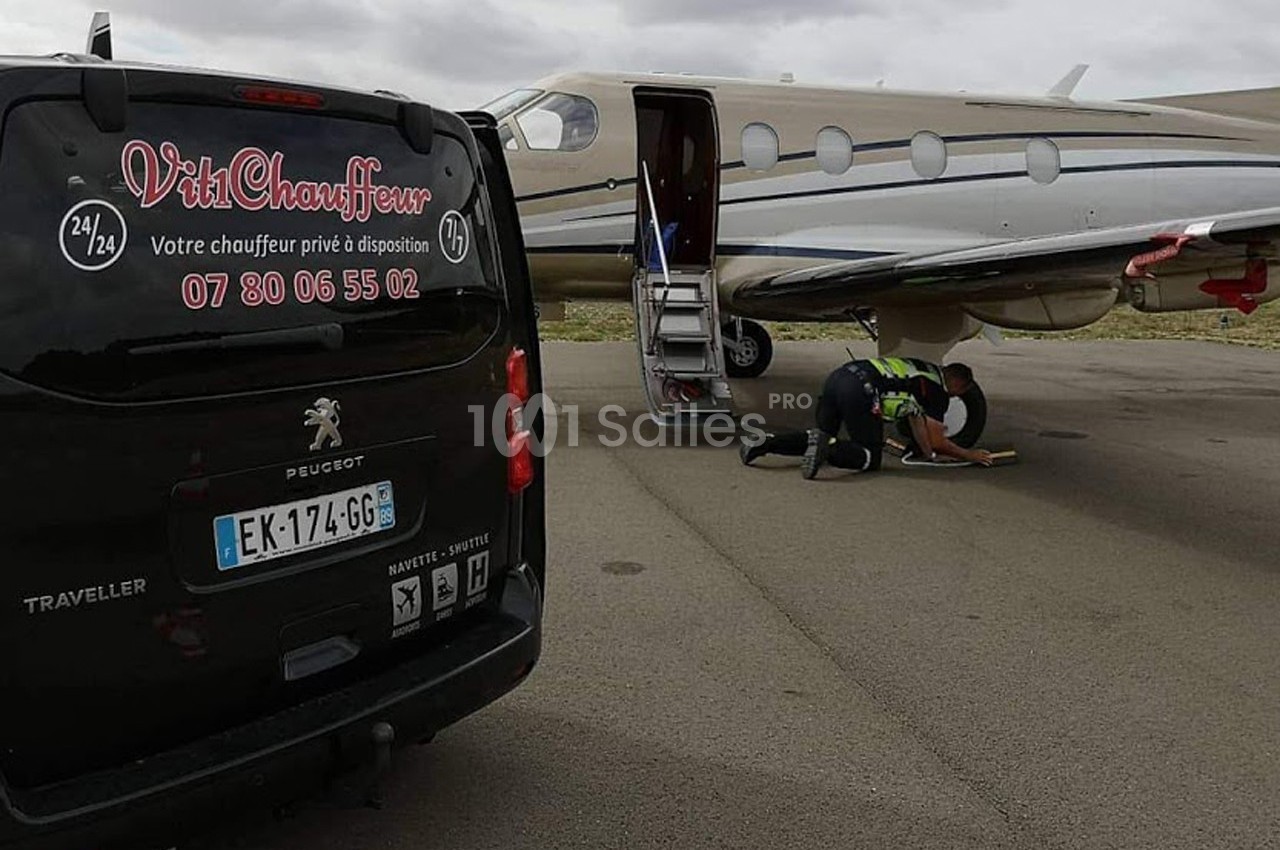 Un van noir stationné près d'un jet privé sur un tarmac, avec une personne agenouillée près de l'avion.