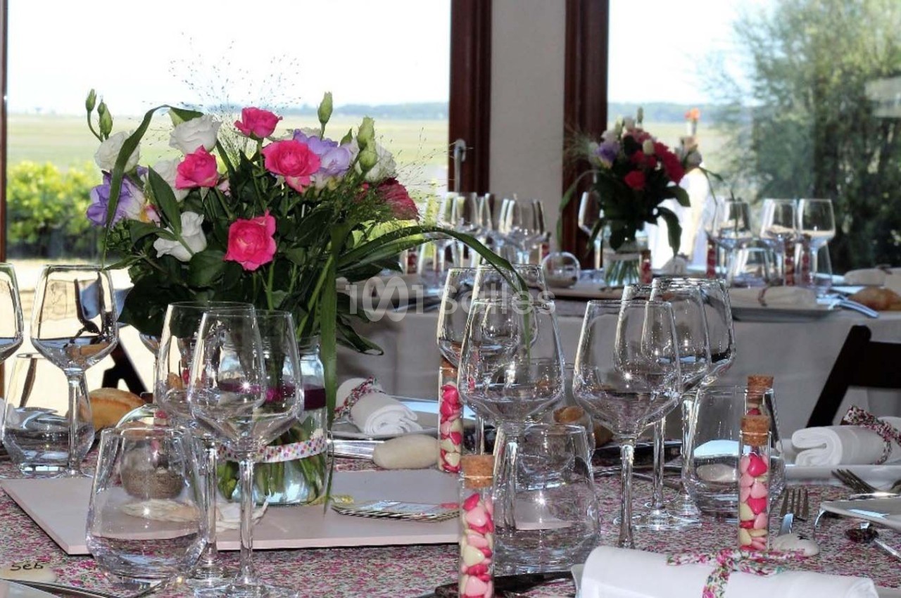 Table élégamment dressée avec des fleurs colorées, verres, serviettes et décorations dans une salle lumineuse avec vue…