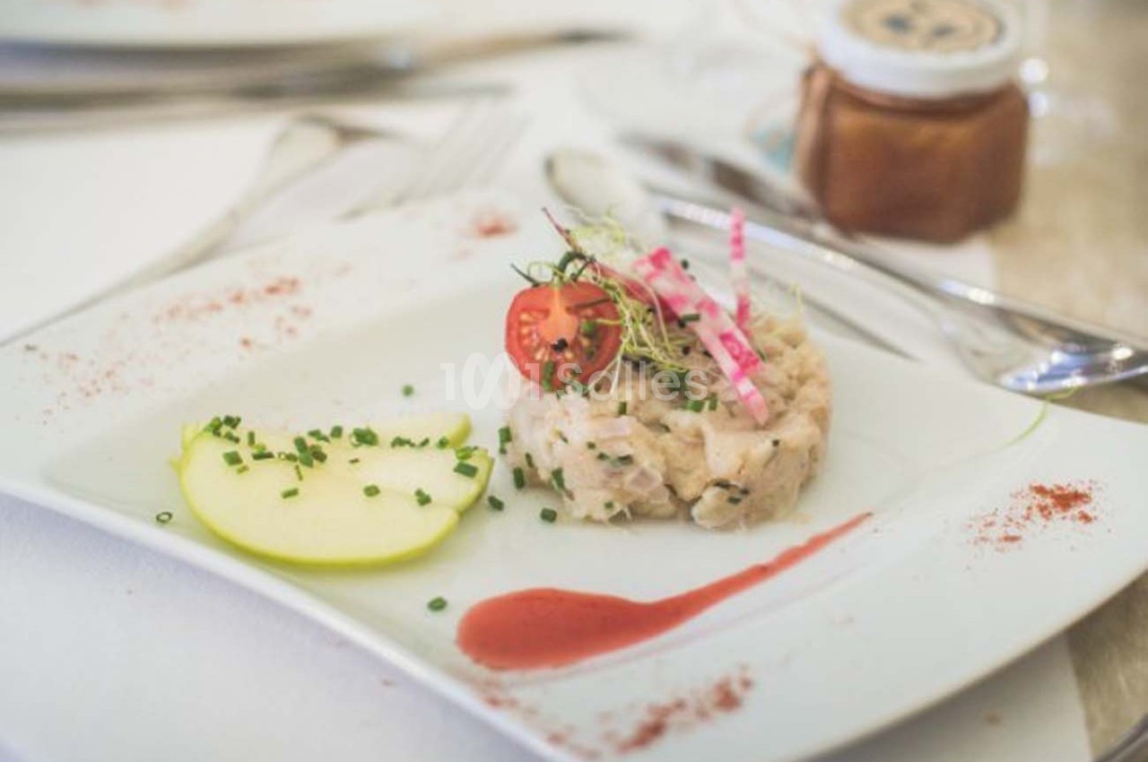 Tartare de poisson servi avec une tranche de pomme, une sauce rouge, des herbes fraîches et des radis sur une assiette…