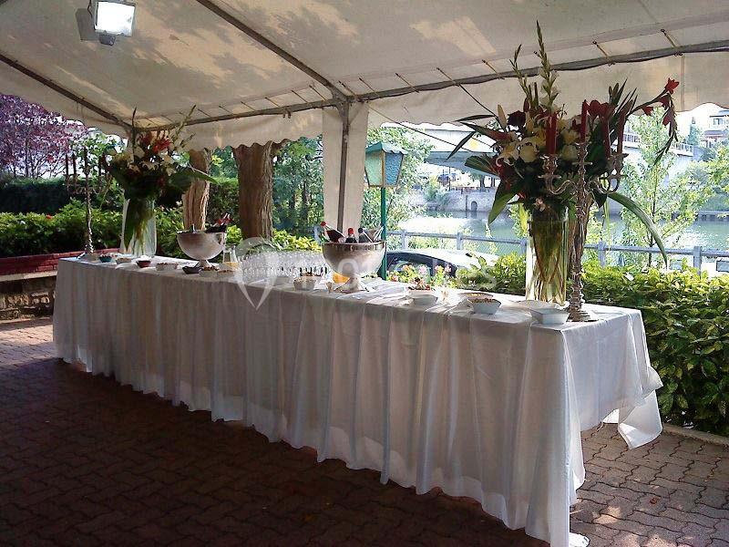 Table dressée sous une tente avec nappes blanches, décorations florales et coupes de champagne près d'un plan d'eau.