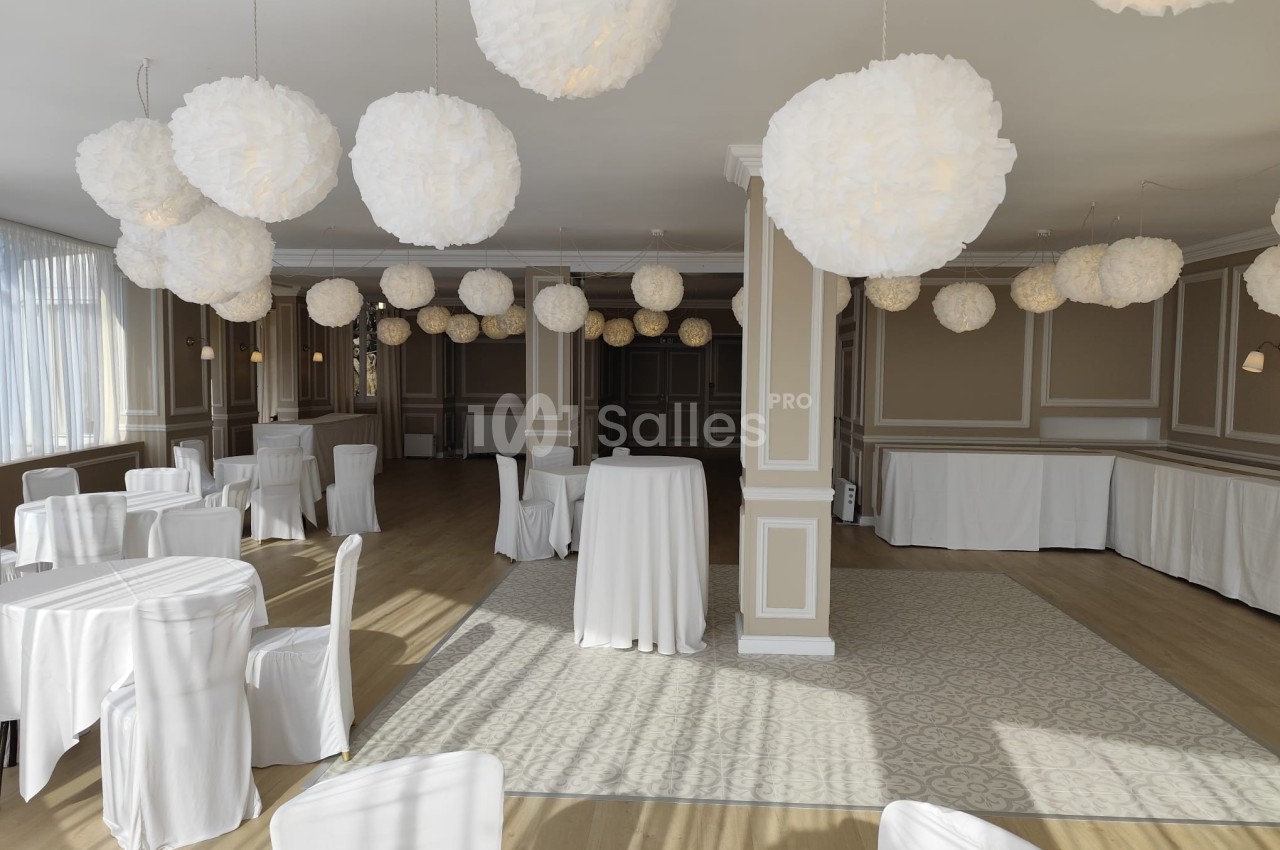 Salle de réception lumineuse avec tables et chaises recouvertes de housses blanches, décorée de suspensions en papier.