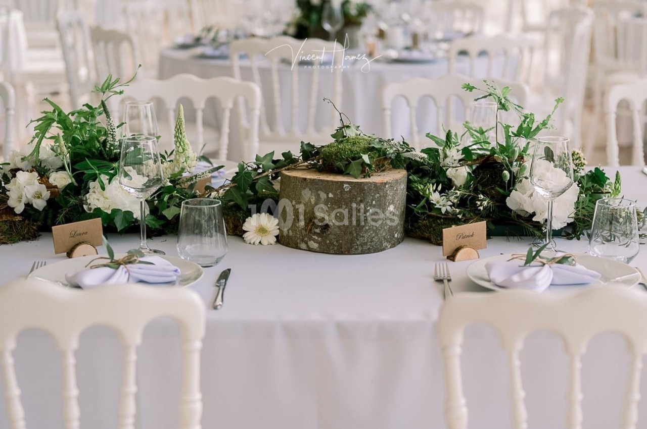 Table décorée avec un centre de table naturel composé de mousse, fleurs blanches et rondin de bois, entourée de vaisselle…
