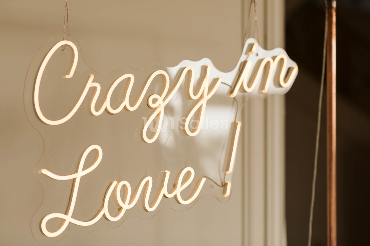 Enseigne lumineuse en néon avec l'inscription ’Crazy in Love !’ suspendue devant une surface vitrée.