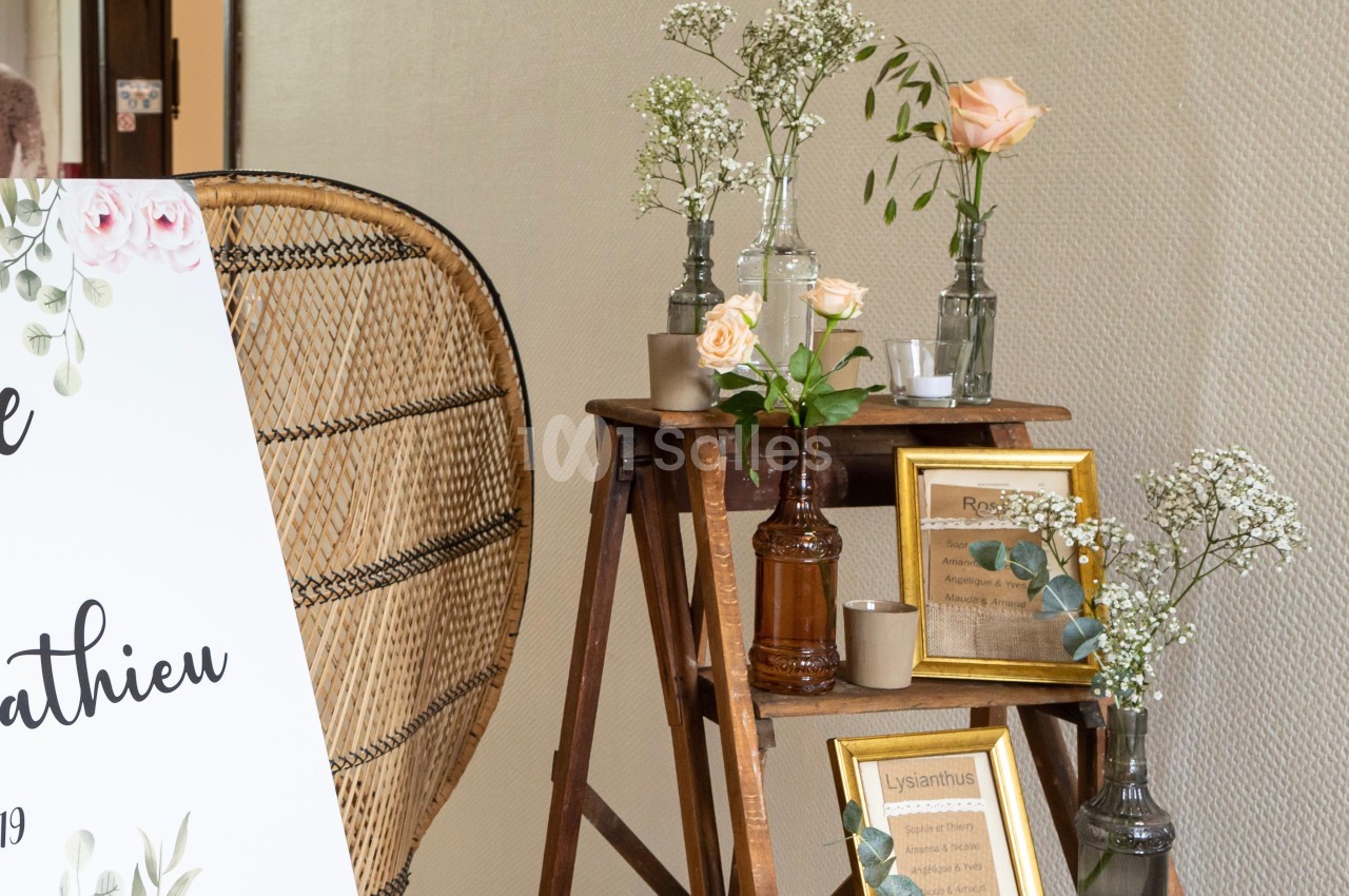 Décoration florale avec roses et gypsophiles sur des vases en verre, disposée sur une échelle en bois près d'un panneau.