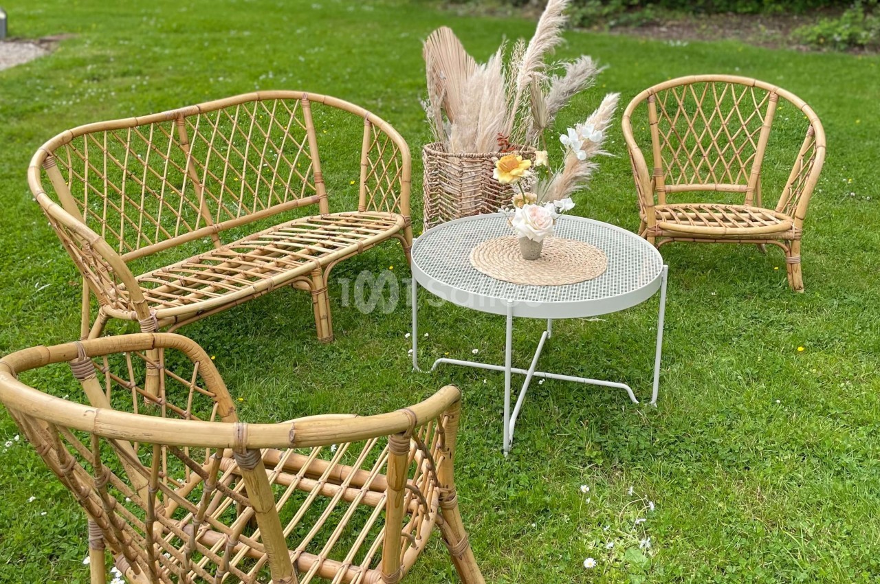 Mobilier en rotin disposé sur une pelouse, avec une table basse blanche et une décoration florale.