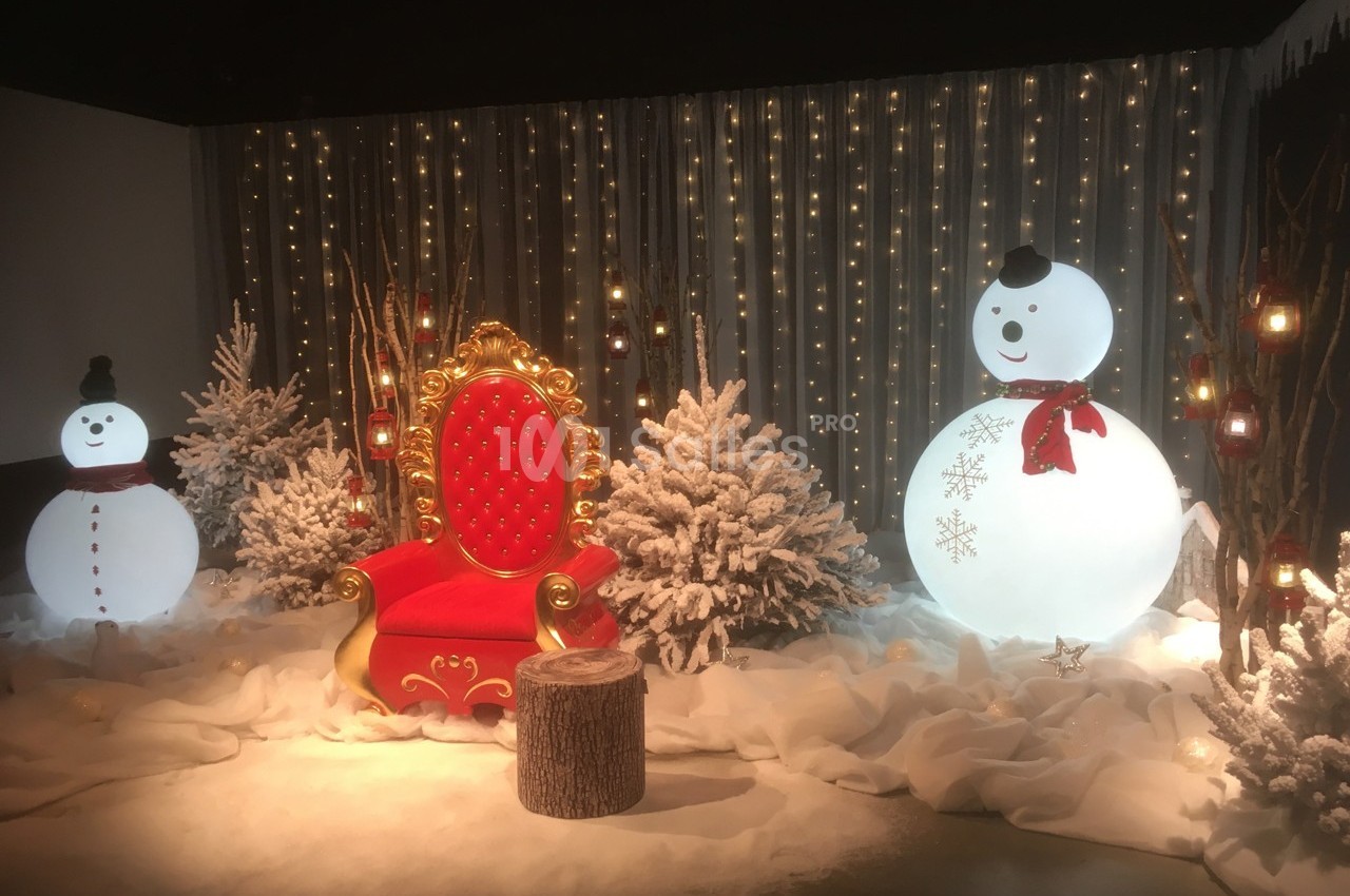 Fauteuil rouge décoratif entouré de bonhommes de neige, sapins enneigés et guirlandes lumineuses dans un décor hivernal.