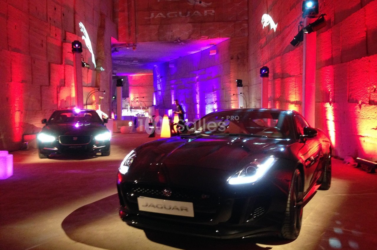 Deux voitures Jaguar exposées dans un espace intérieur éclairé par des lumières rouges et violettes.