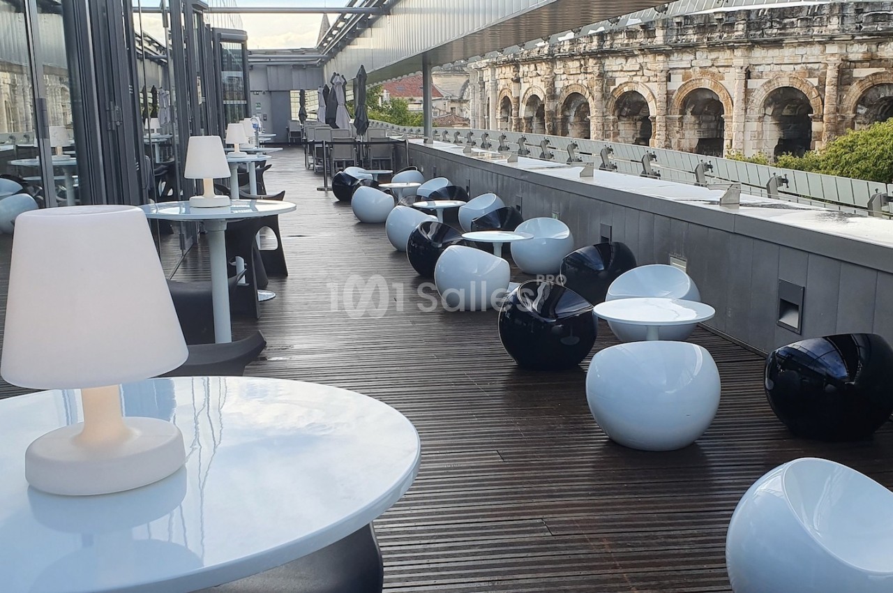 Terrasse moderne avec mobilier design, tables et sièges arrondis, vue sur un amphithéâtre ancien en arrière-plan.