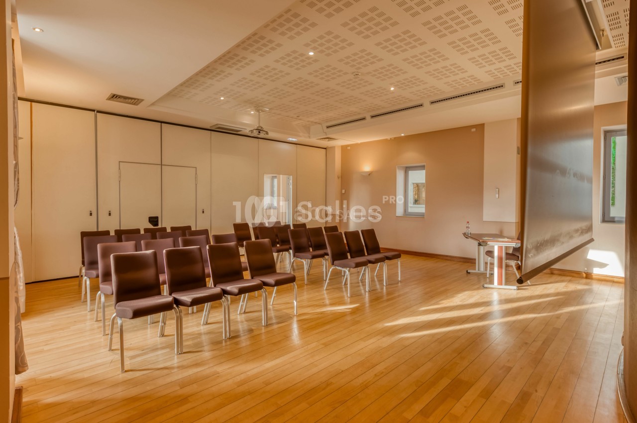 Salle de réunion lumineuse avec parquet en bois, chaises alignées et cloisons modulables.