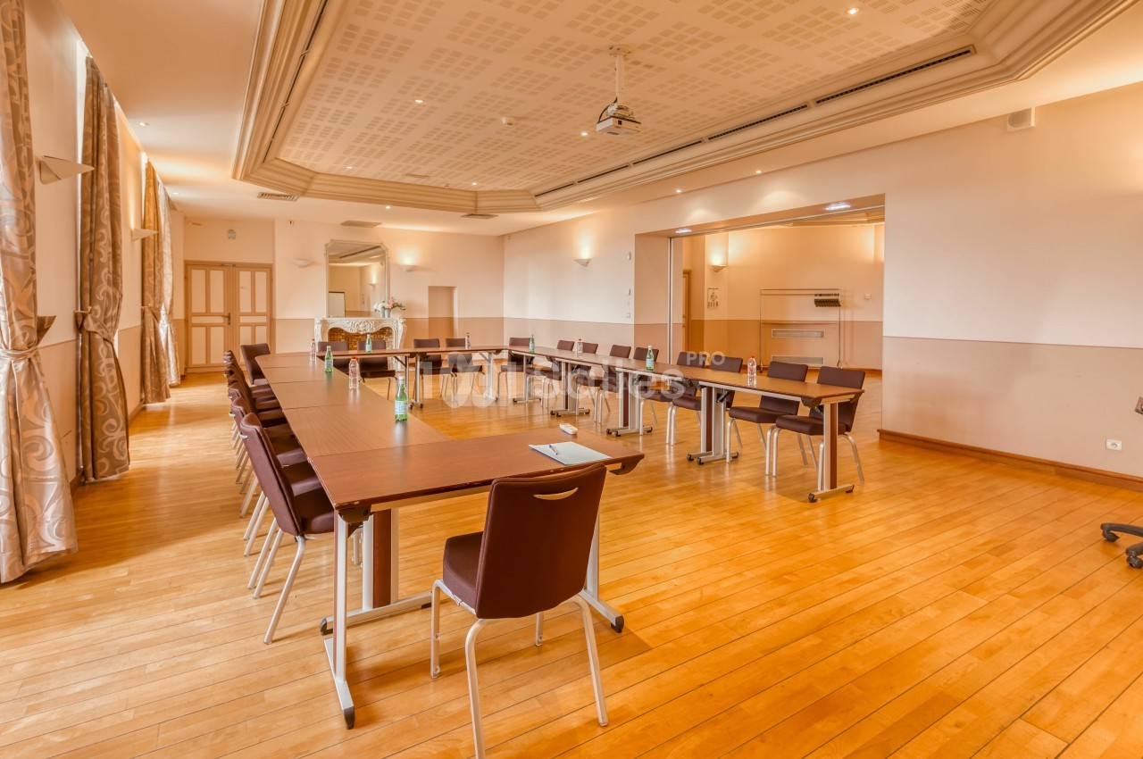 Salle lumineuse avec parquet, tables disposées en U, chaises marron et équipement de projection au plafond.