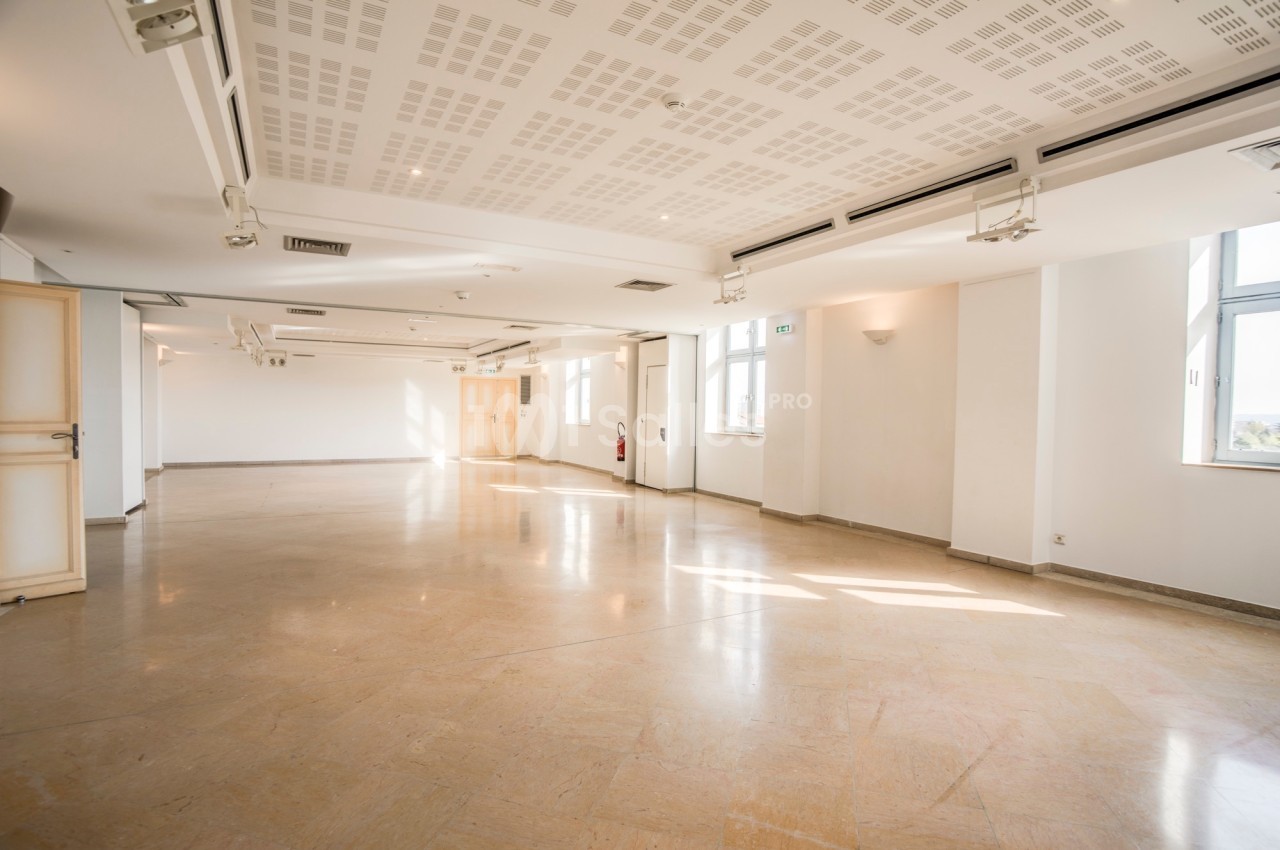 Salle lumineuse vide avec un sol en marbre, des murs blancs, un plafond avec spots et des fenêtres laissant entrer la…