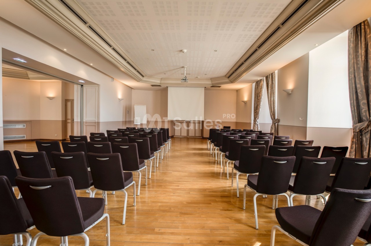 Salle de conférence vide avec des rangées de chaises noires, un écran de projection et un tableau blanc à l'arrière.