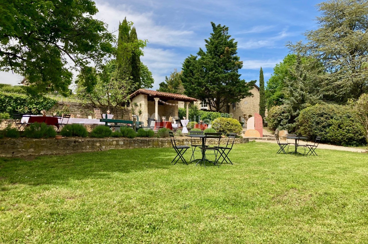 Jardin verdoyant avec tables et chaises en métal noir, entouré de végétation et de bâtiments en pierre.