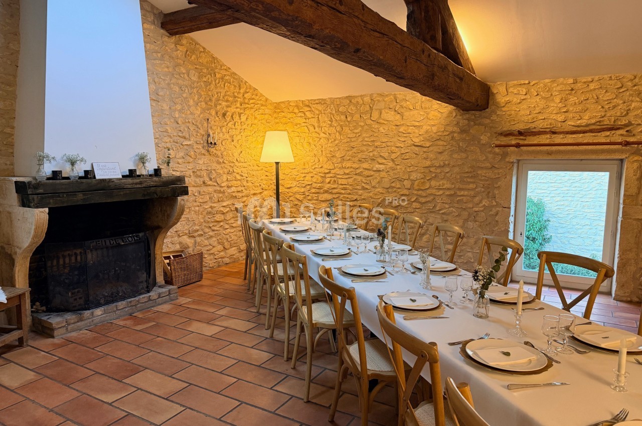 Table dressée pour un repas dans une salle rustique avec murs en pierre, poutres apparentes et cheminée.