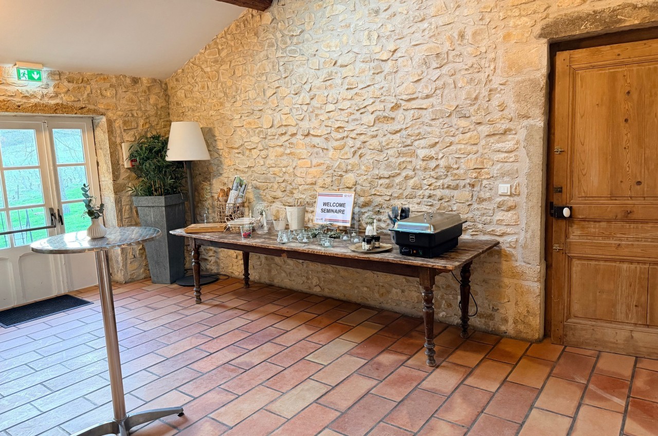Table en bois avec des objets décoratifs, posée contre un mur en pierre dans une pièce lumineuse au sol en terre cuite.
