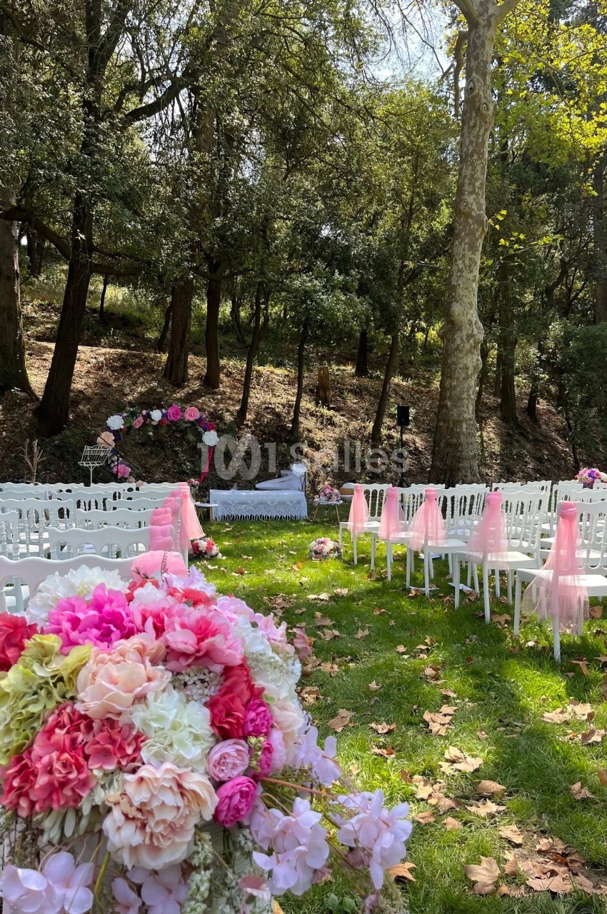 Chaises blanches alignées sur une pelouse avec des décorations florales roses, prêtes pour une cérémonie en plein air.