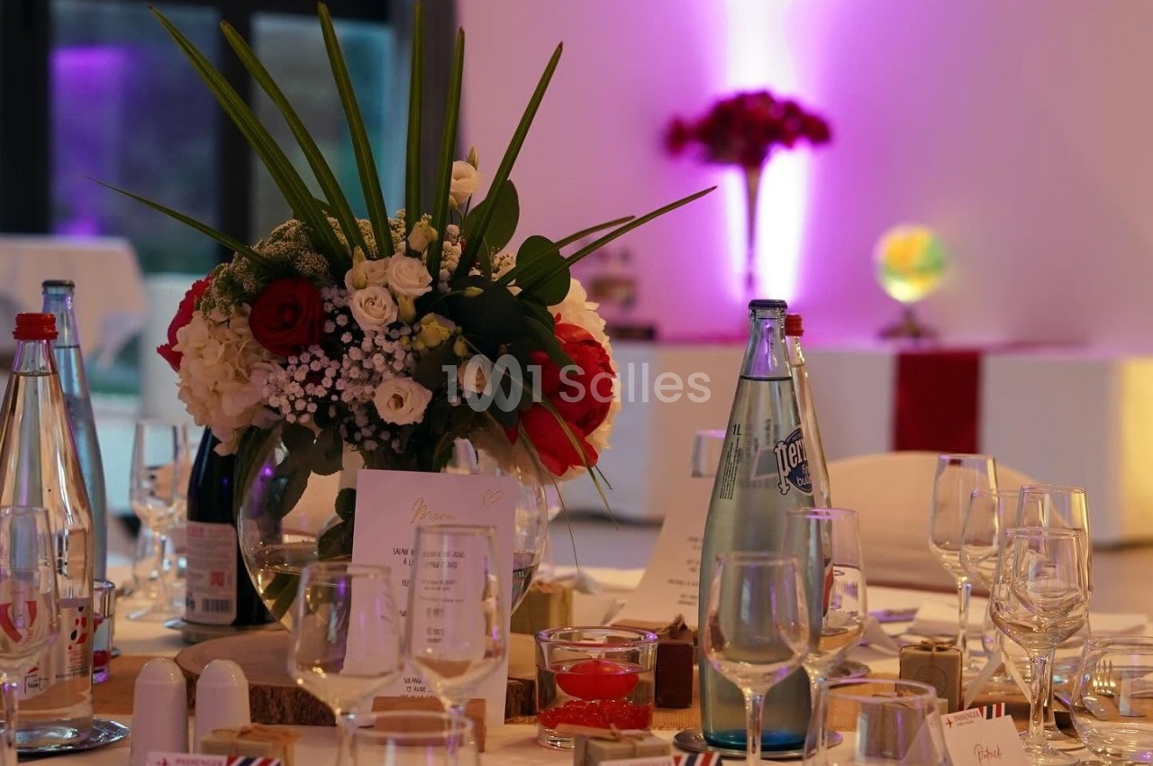 Table de réception élégamment dressée avec des fleurs, verres, bouteilles d'eau et lumière d'ambiance violette en arrière…
