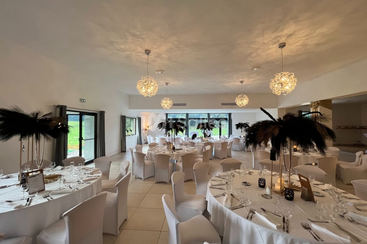 Salle de réception élégamment décorée avec des tables rondes, nappes blanches et centres de table à plumes noires.