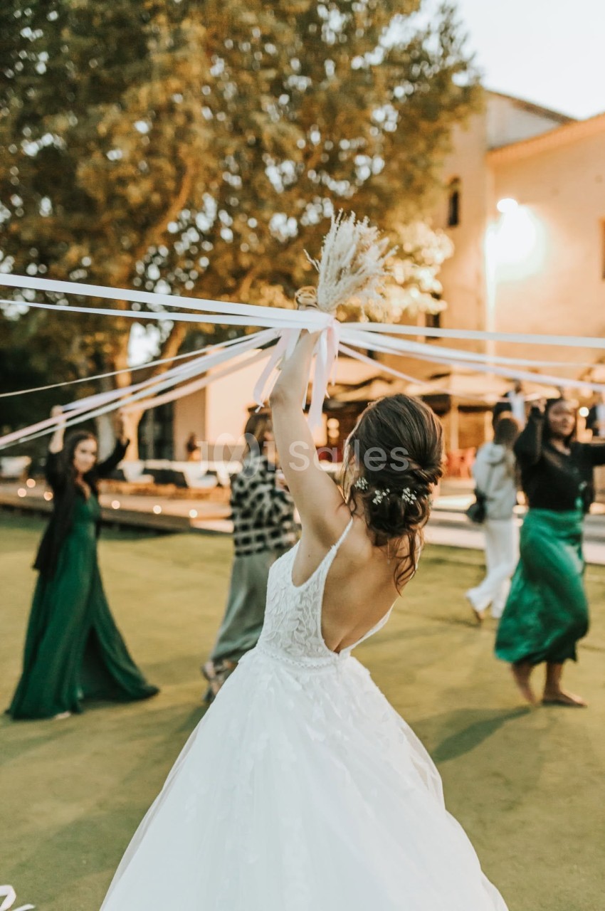 Une mariée en robe blanche danse en extérieur, tenant des rubans entourée d'invités en tenue de soirée.