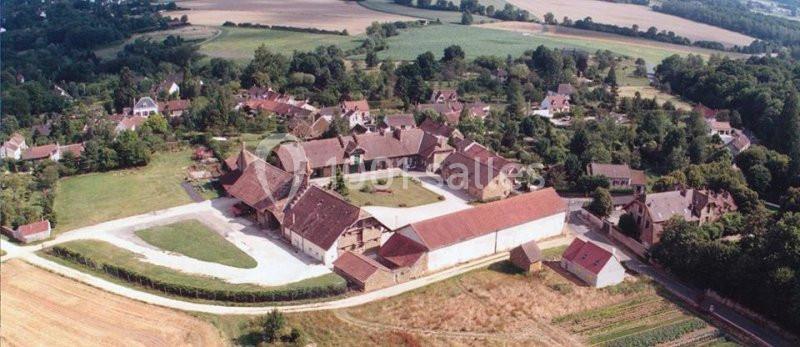Vue aérienne d'un village rural avec des bâtiments en pierre, des toits en tuiles et des champs environnants.