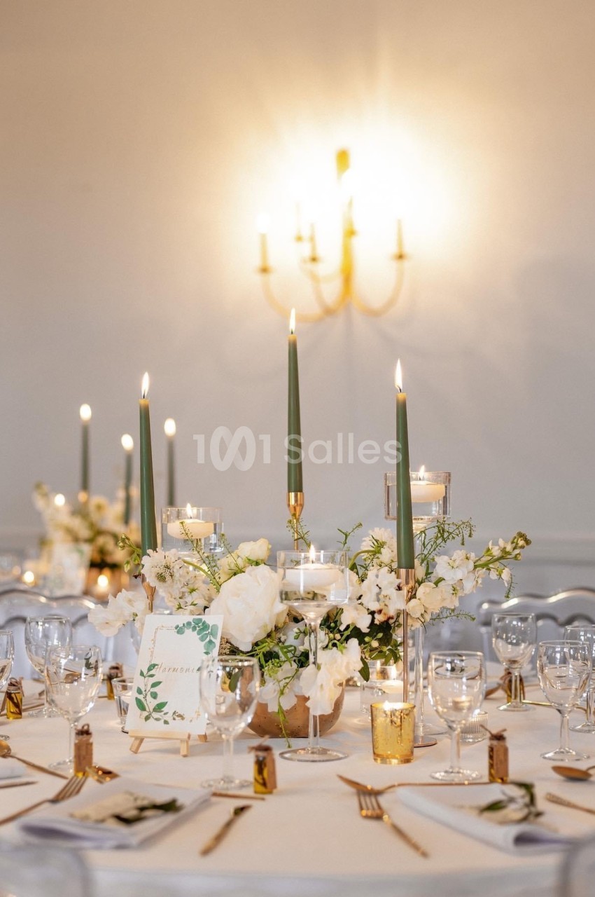 Table élégamment dressée avec chandeliers verts, fleurs blanches et décoration raffinée dans une ambiance lumineuse.