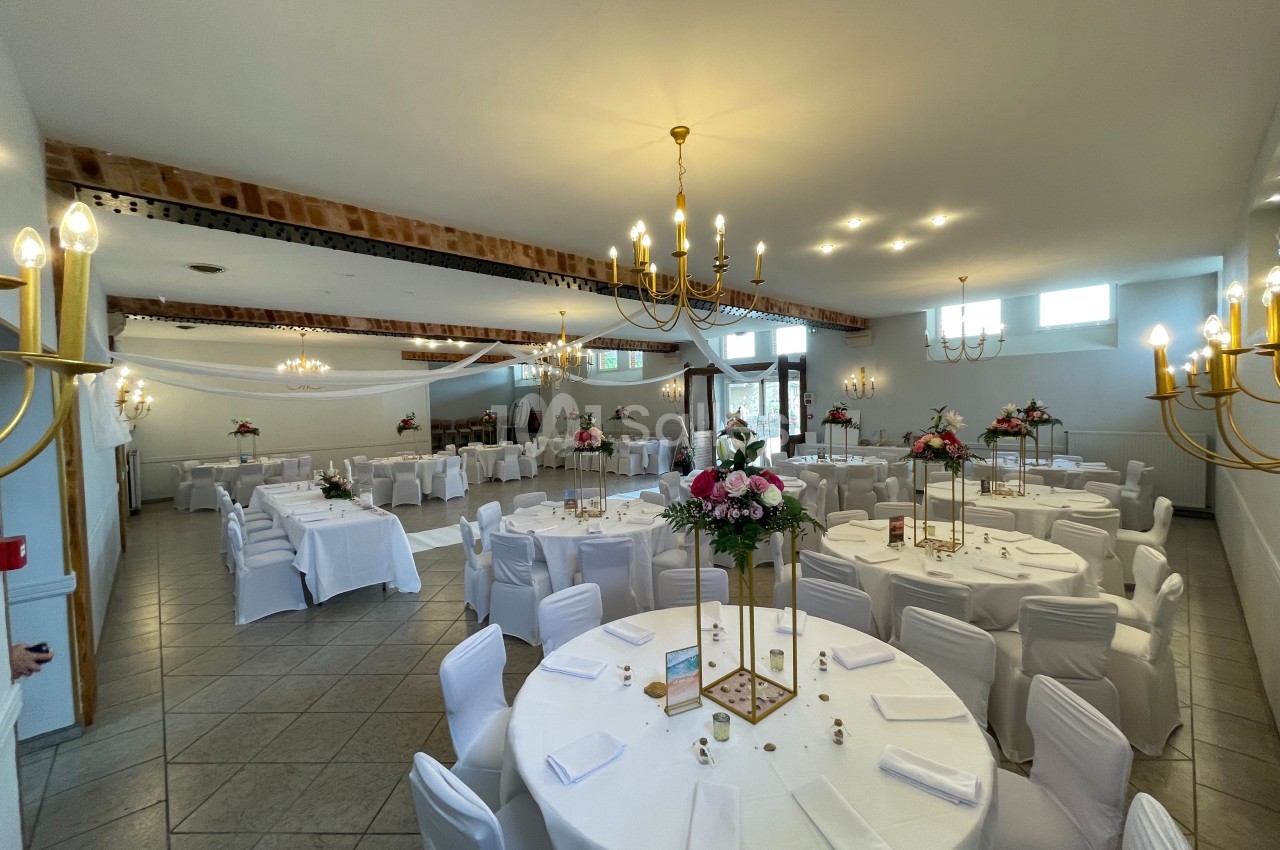 Salle de réception lumineuse avec tables rondes décorées de nappes blanches et centres de table fleuris.