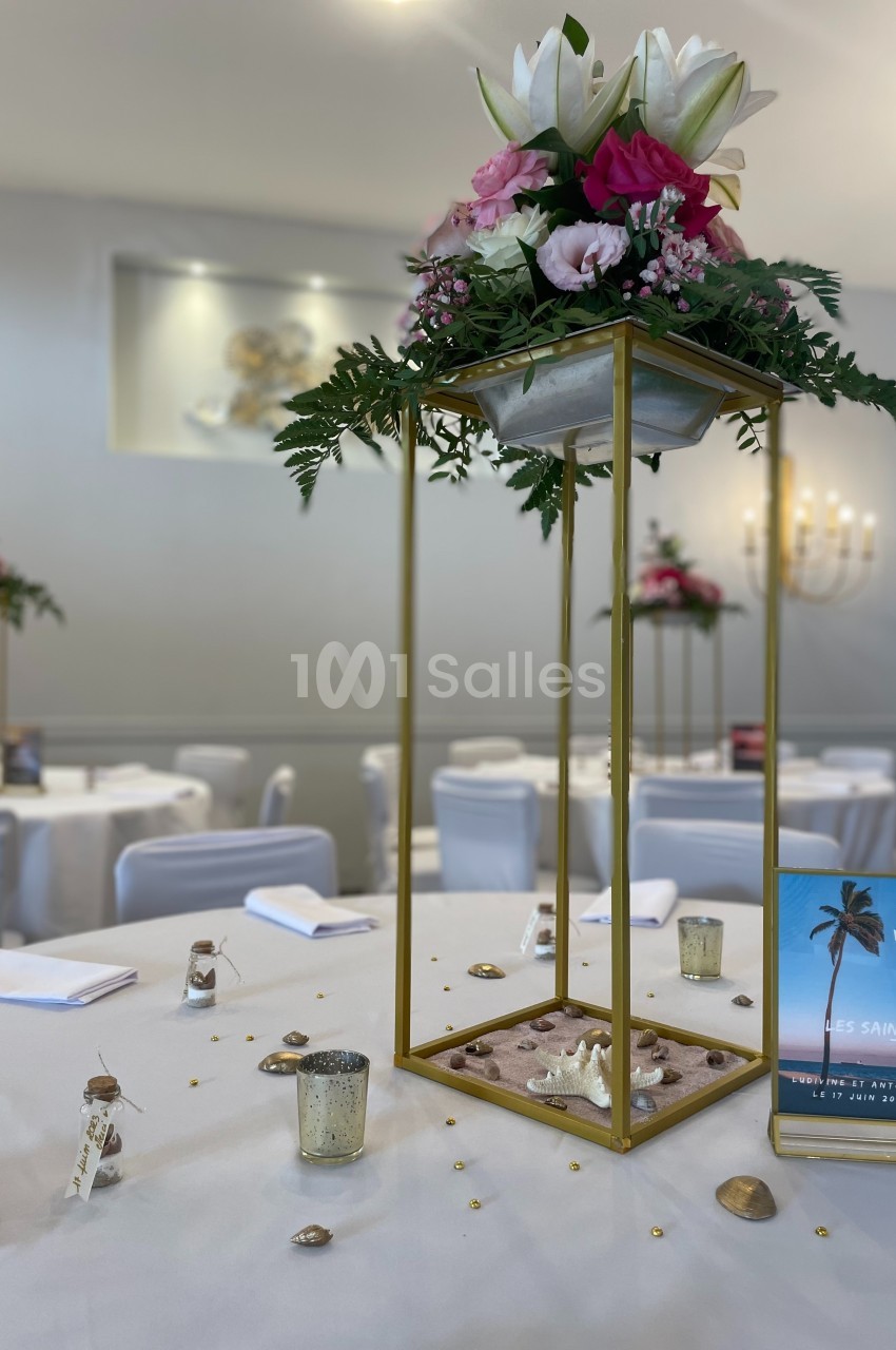 Centre de table floral avec structure dorée, décoré de fleurs roses et blanches, sur une table dressée pour un événement.