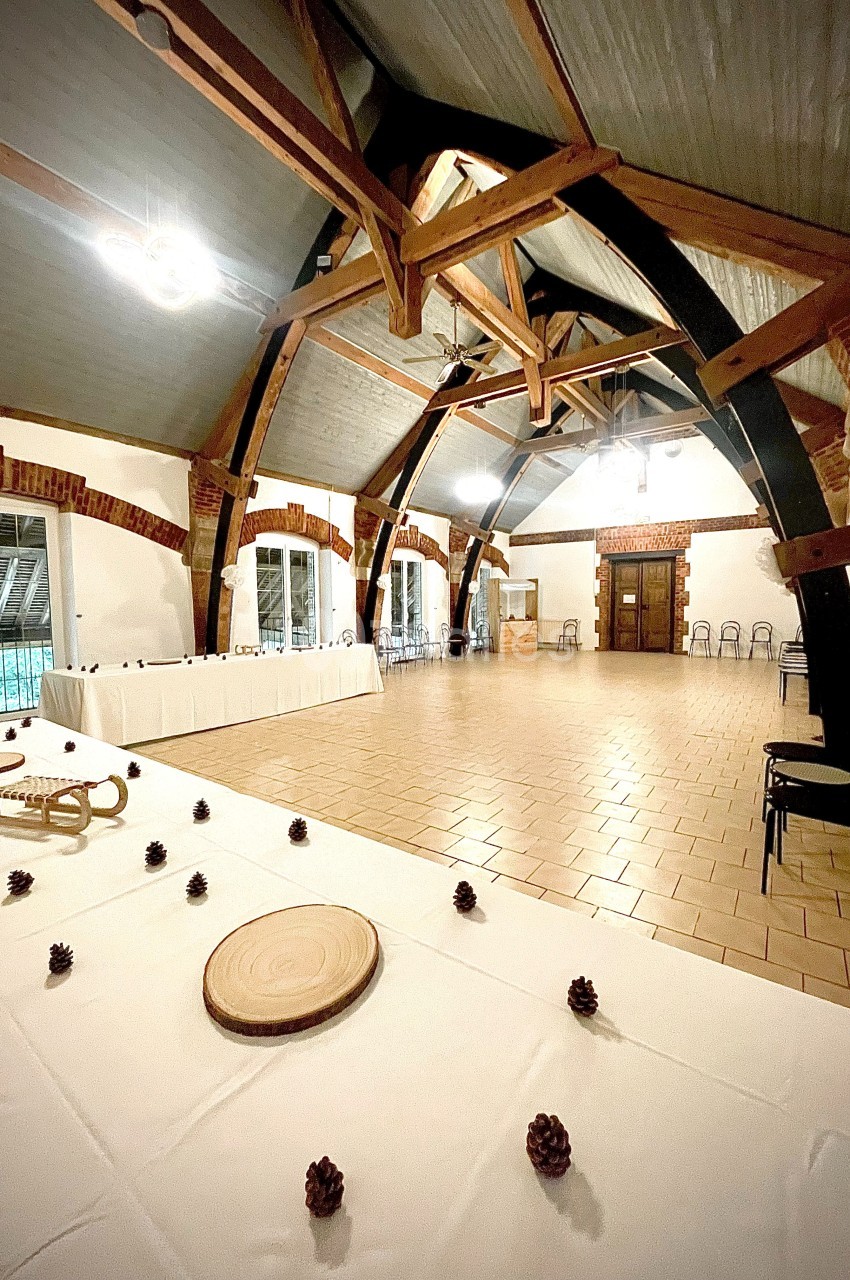 Salle spacieuse avec charpente en bois apparente, tables décorées de pommes de pin et grandes fenêtres donnant sur l…