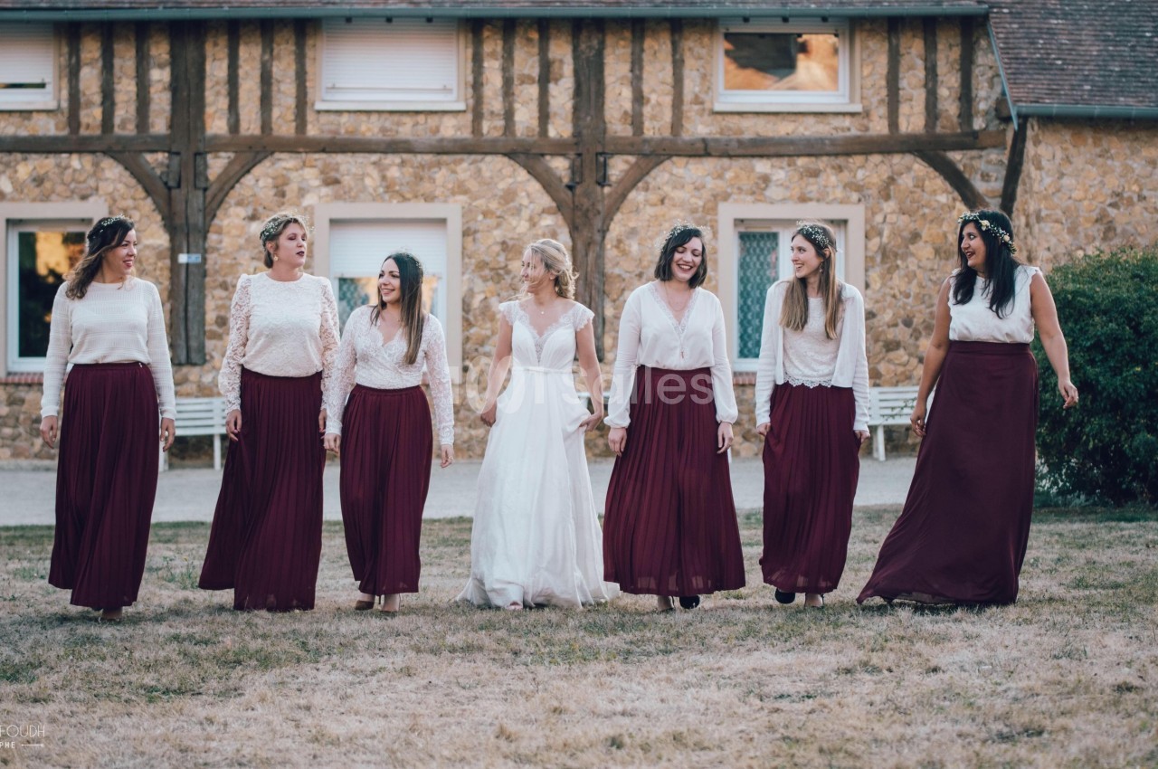Un groupe de femmes, dont une en robe blanche, marche sur une pelouse devant un bâtiment en pierre et bois.