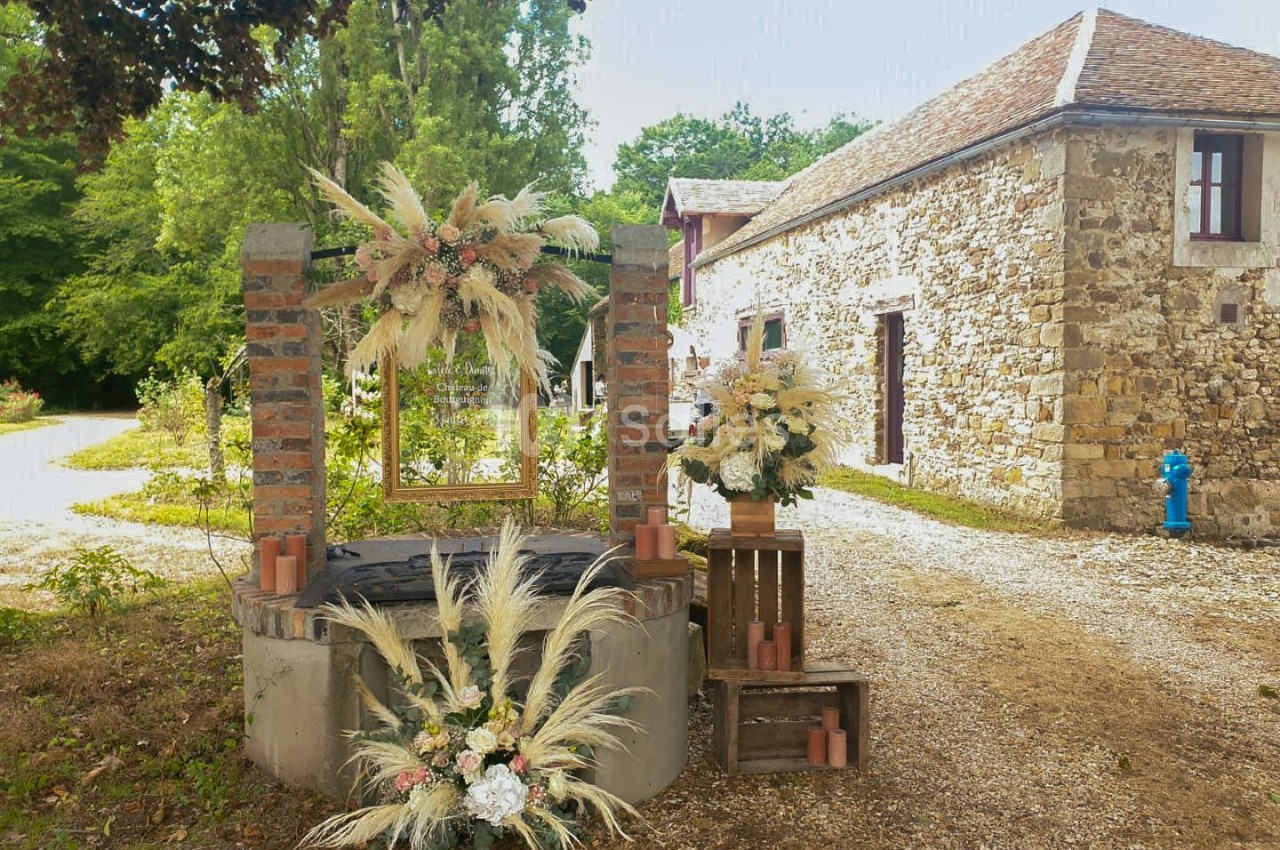 Décoration florale avec des herbes séchées et des fleurs autour d'un puits en pierre, près d'une maison en pierre.