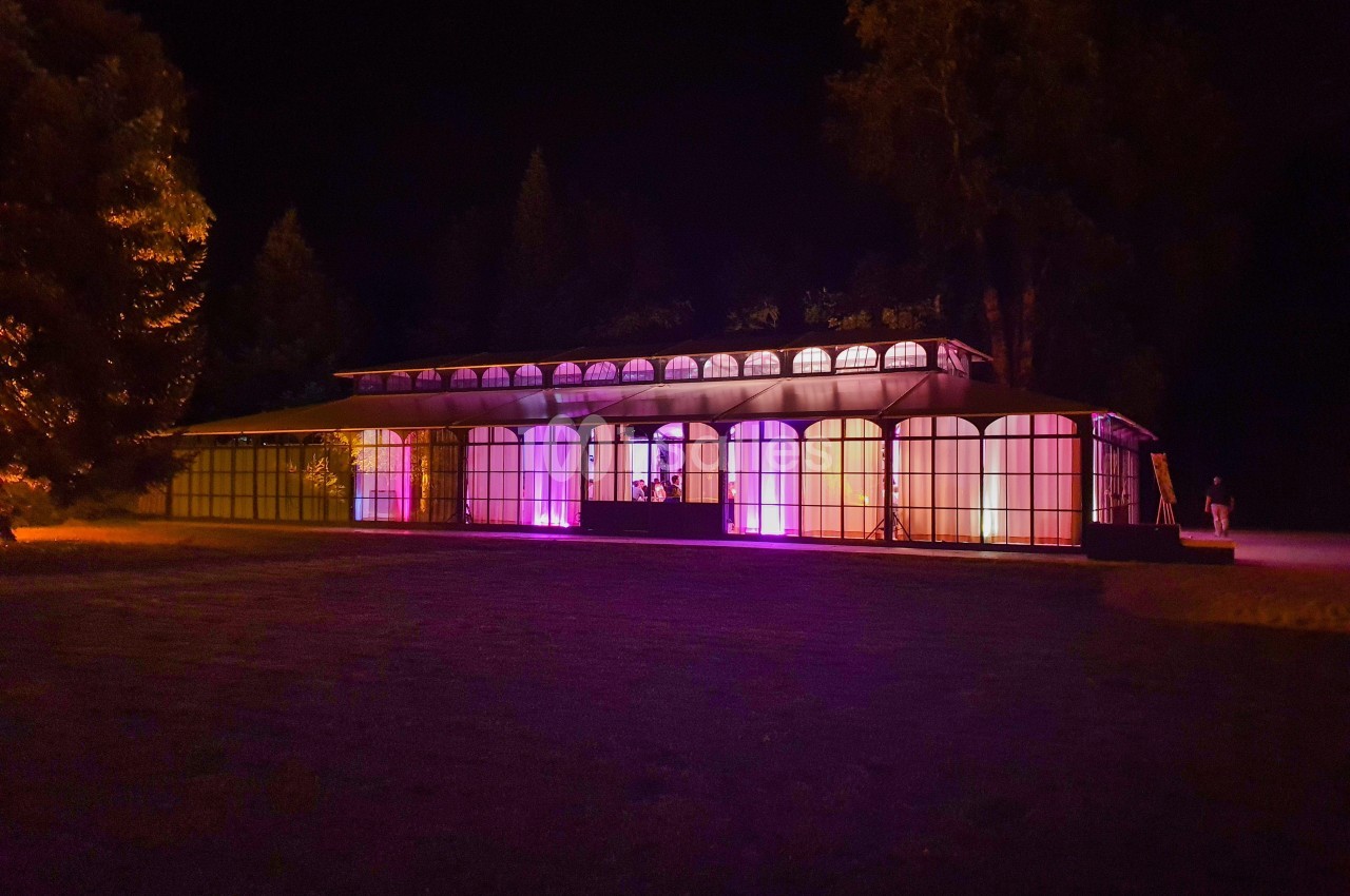 Bâtiment vitré illuminé par des lumières colorées dans un environnement extérieur nocturne.