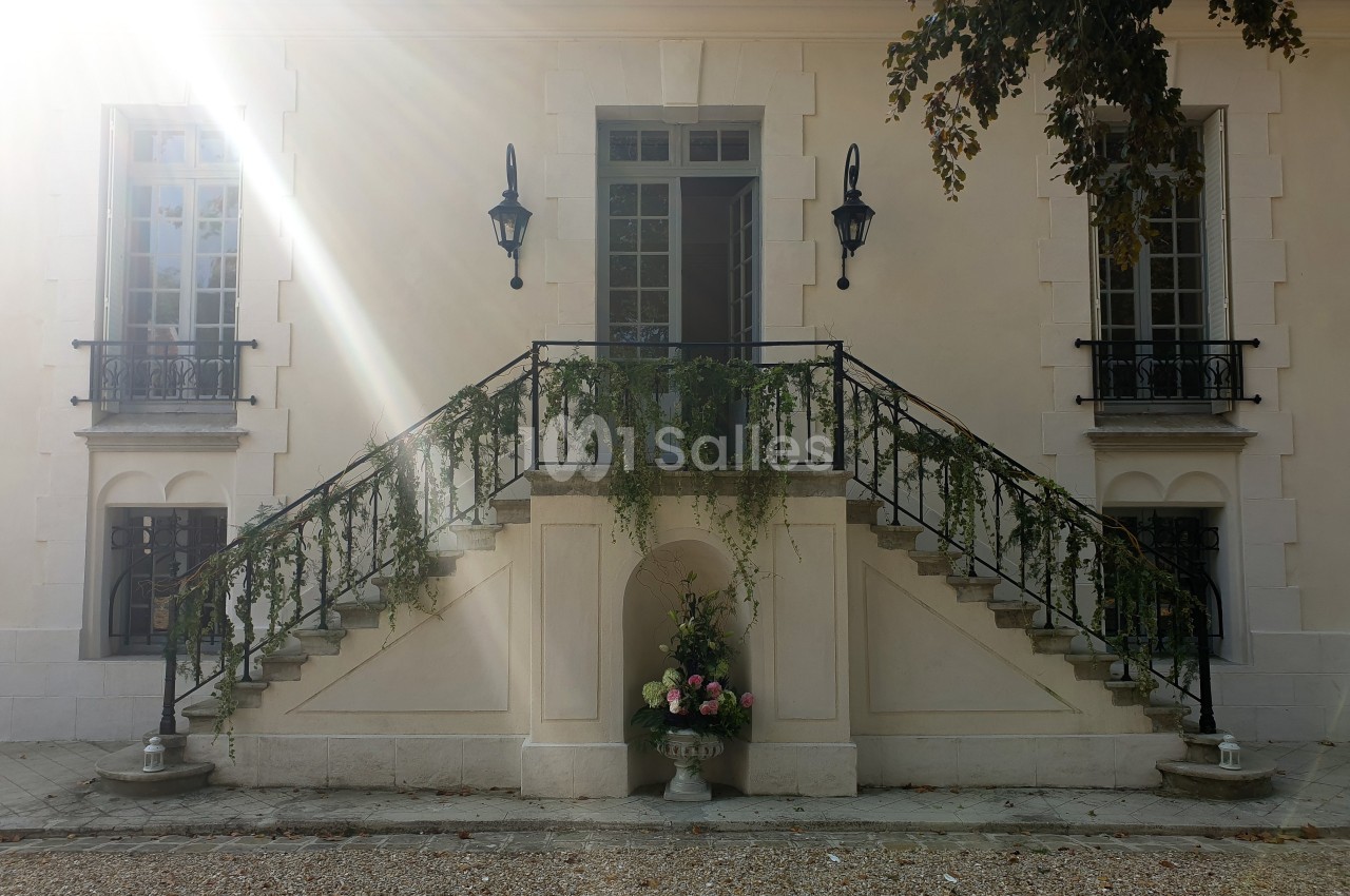 Façade d'un bâtiment avec un escalier symétrique orné de plantes grimpantes et un vase de fleurs au centre.