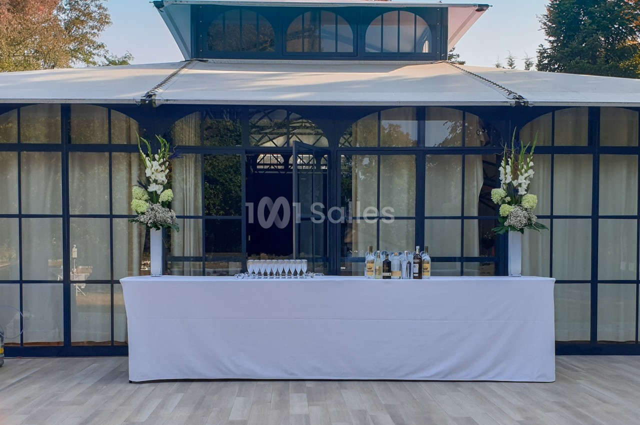 Table dressée avec nappage blanc, décorée de fleurs et disposée devant une structure vitrée dans un espace extérieur.